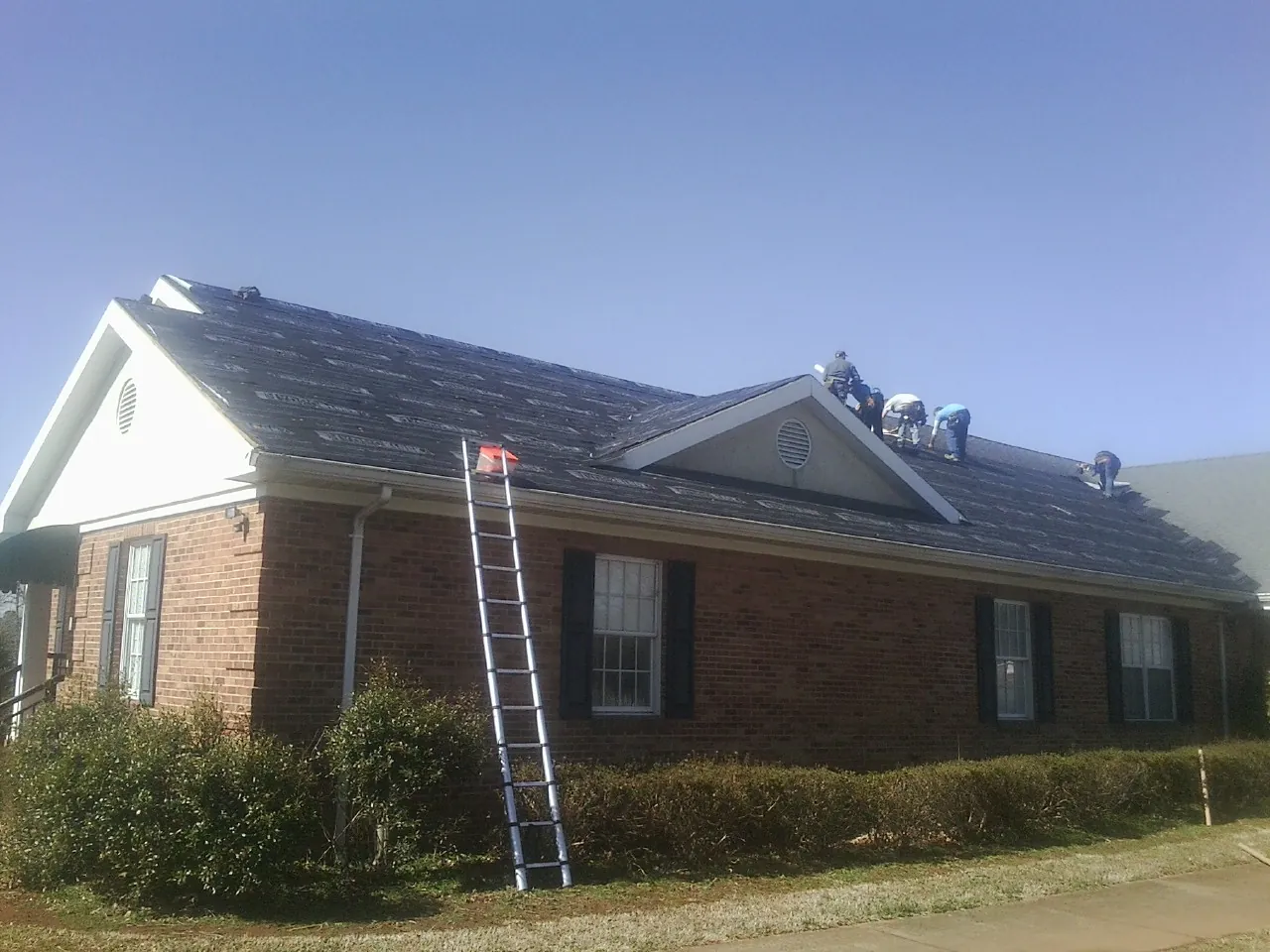 Crew tearing shingles off a brick ranch roof with a ladder set — Metal Roof Repair work by our crew in Port Jervis