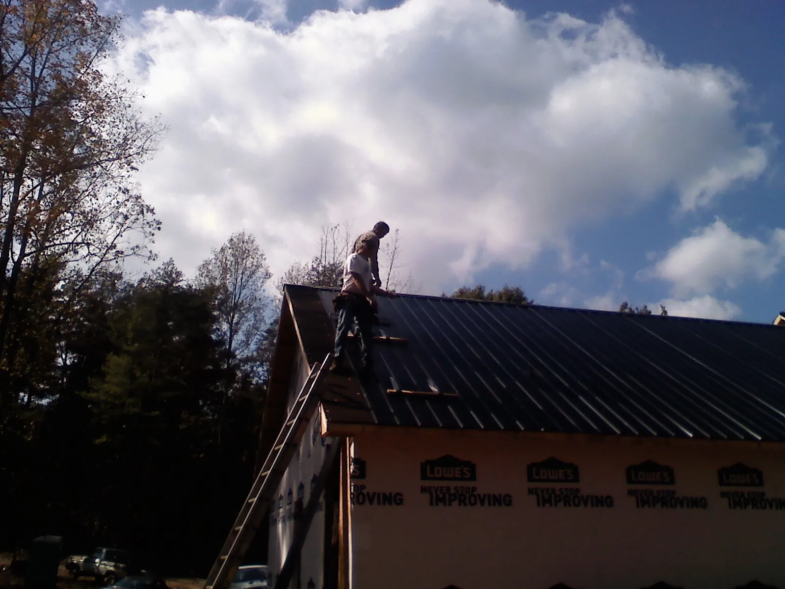 Roofer fastening dark metal panels high against a cloudy sky, from a Roof Inspection job in Port Jervis