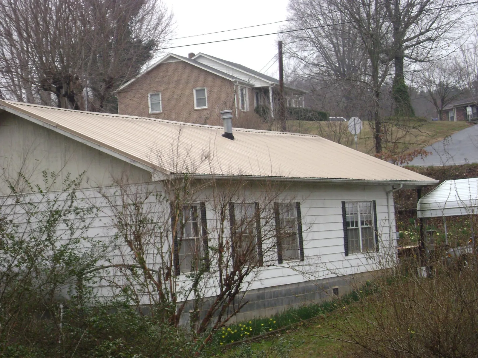 Tan metal roof on a white sided house set into a hillside — Commercial Roofing by Roofing Brothers in Port Jervis